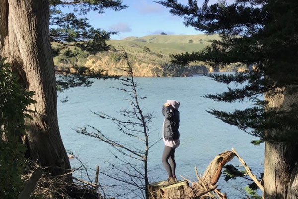 Alanah Vellone standing on a stump between trees with a lake in the background