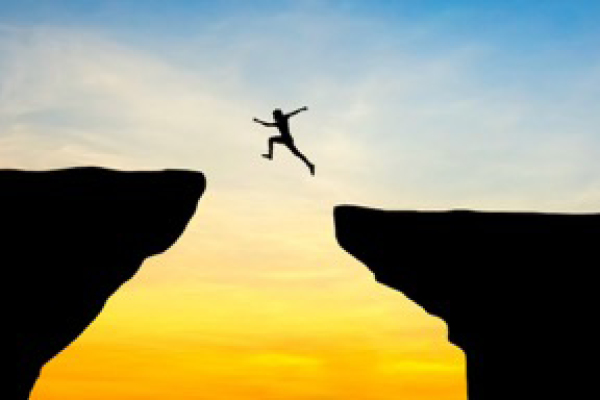 silhouette of person leaping between two cliffs