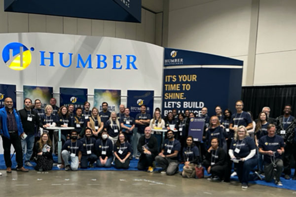 large group of humber faculty in front of a Humber booth