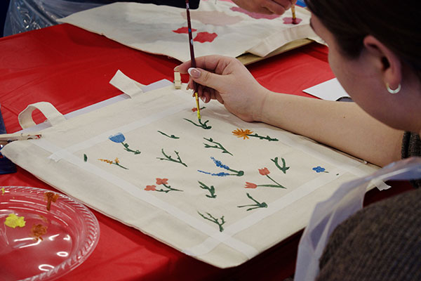 person painting flowers on a tote