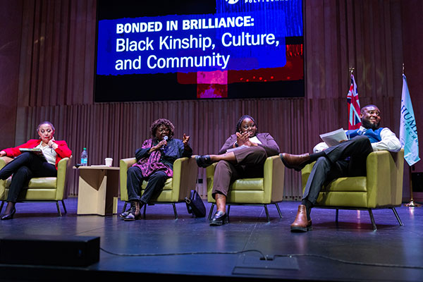 Four individuals sit on a stage during a discussion panel titled "Bonded in Brilliance: Black Kinship, Culture, and Community."