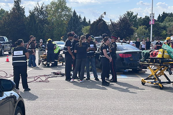 Emergency responders and bystanders are gathered in a parking lot near a black car.