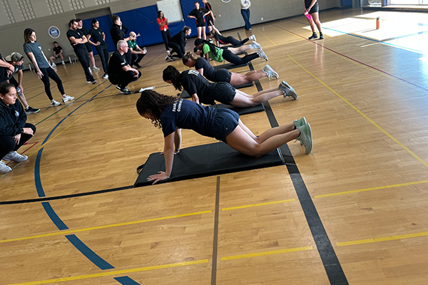 People in a gym engage in group exercise, performing plank positions on mats.