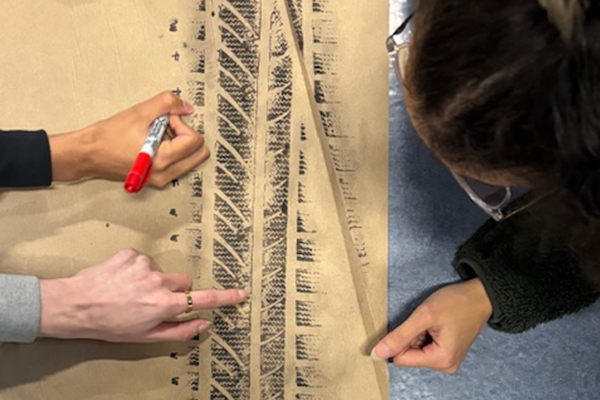 individuals examine a large tire tread pattern on paper.