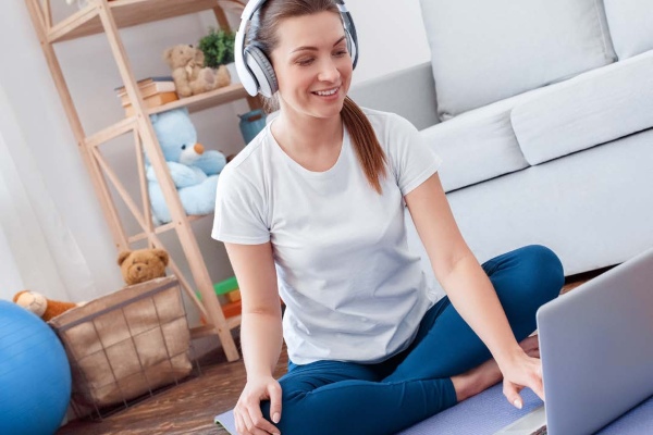 woman sitting on a yoga mat with headphones on and her laptop